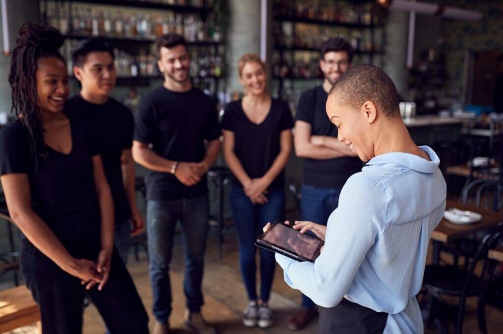 Female Restaurant Manager With Digital Tablet Giving Team Talk To Waiting Staff